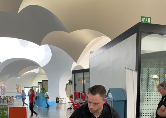 Man toont truc met elastiek aan twee kinderen in moderne hal met boogvormig plafond. (vergroot foto)