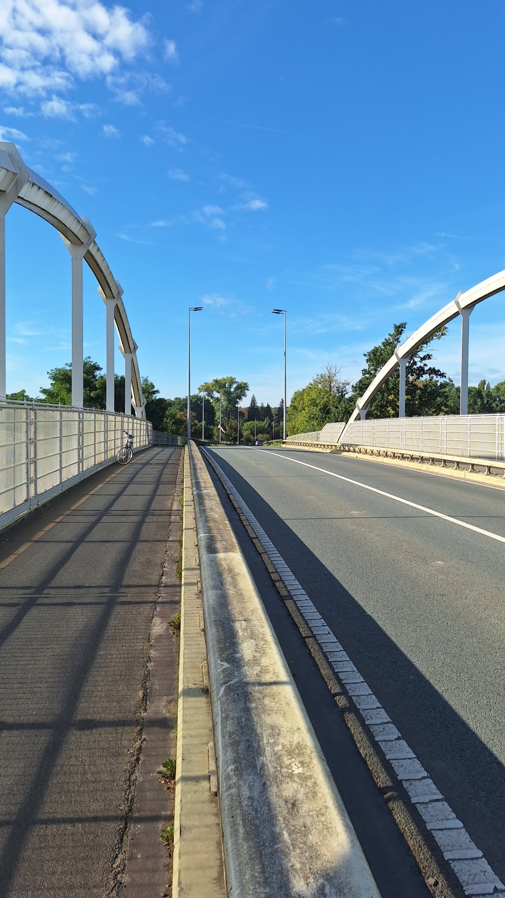 Brug met fietspad en weg, blauwe lucht en schaduwen van hekwerk op het fietspad.