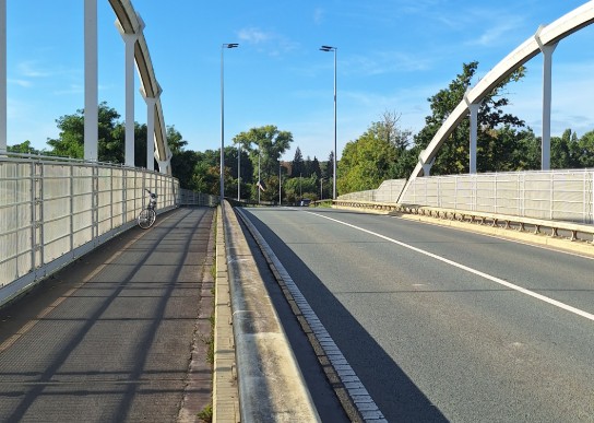 Brug met fietspad en weg, blauwe lucht en schaduwen van hekwerk op het fietspad. (vergroot foto)