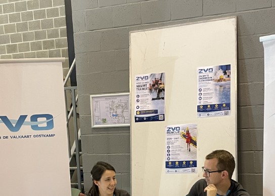 Twee mensen zitten achter een tafel met folders en promotiemateriaal van zwemclub ZVO. (vergroot foto)