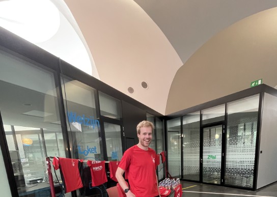 Man in rode sportshirt met badmintonracket in moderne hal met glazen wanden en sportkleding. (vergroot foto)