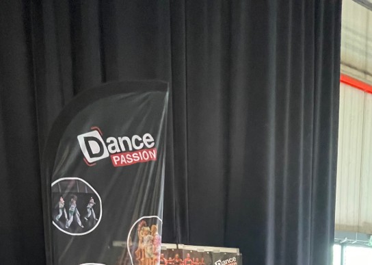 Twee vrouwen praten met twee jonge dames bij een Dance Passion infostand met banners en flyers. (vergroot foto)