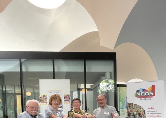 Vier senioren staan lachend bij een informatiestand en steken hun duimen omhoog. (vergroot foto)