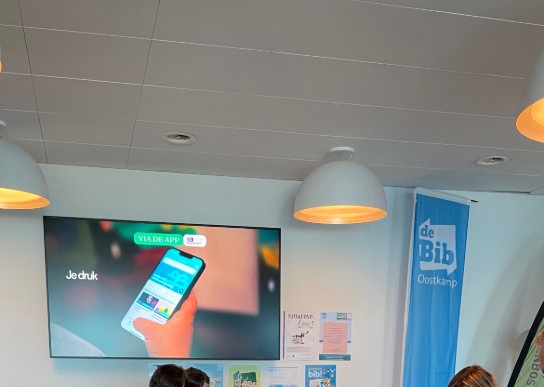 Mensen spelen een bingospel in een bibliotheek met informatie en scherm over een app op de achtergrond. (vergroot foto)