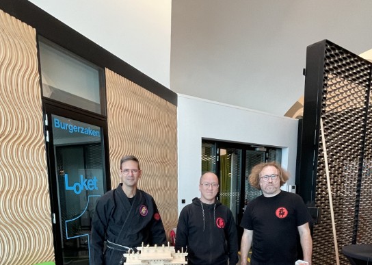 Drie mannen bij een tafel met Japanse wapens en een houten tempelmodel, banner met Japanse tekens. (vergroot foto)