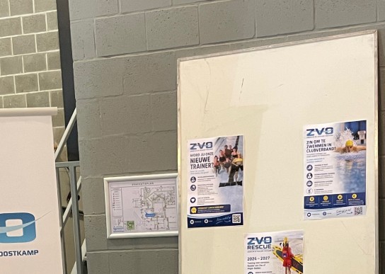 Twee mensen zitten achter een tafel met folders en flyers van zwemvereniging ZVO Oostkamp. (vergroot foto)