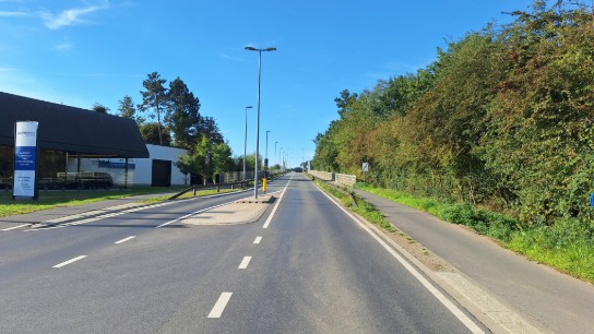 Een lege weg met fietspad naast groene bomen en een gebouw aan de linkerkant. (vergroot foto)
